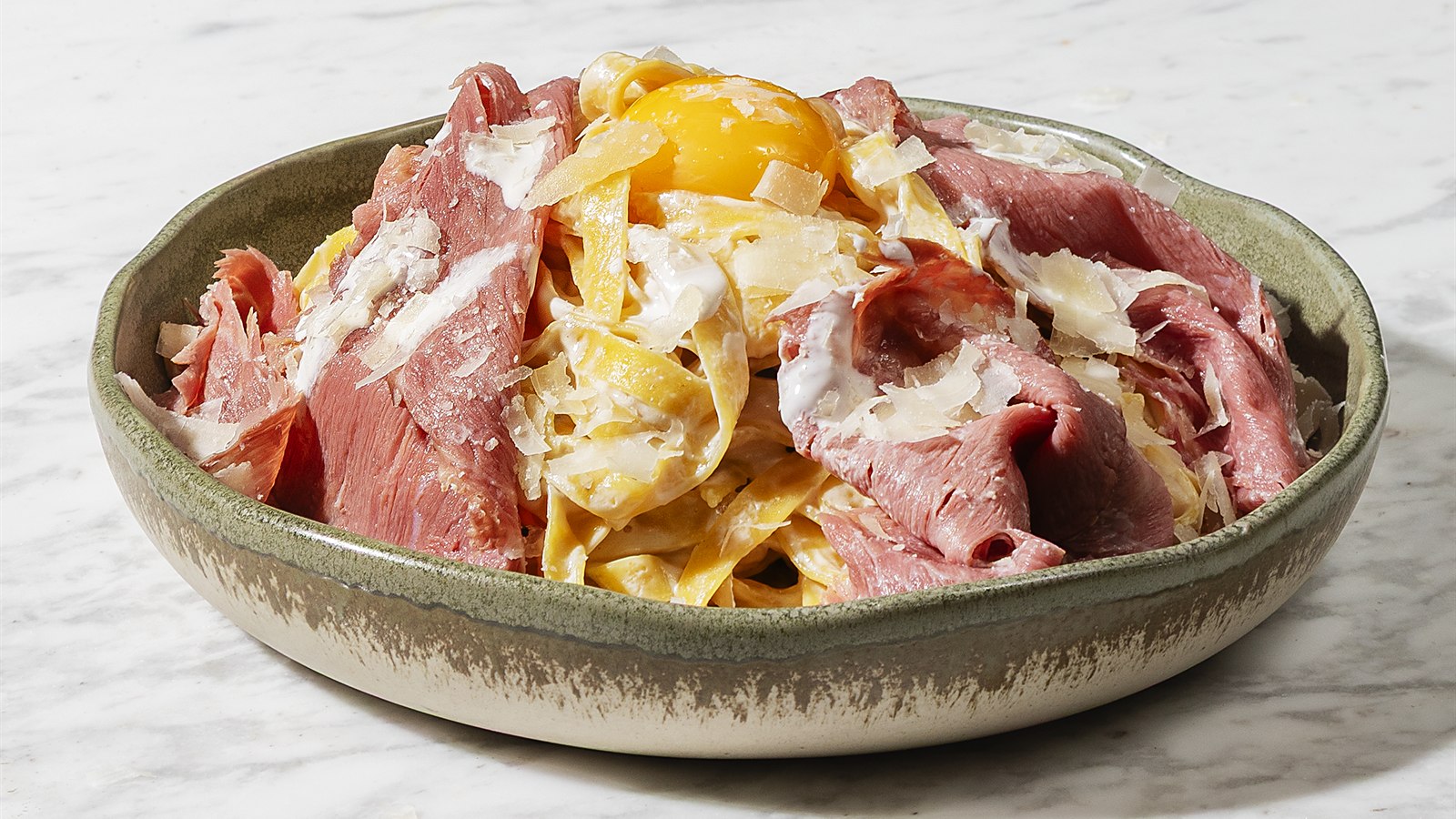 HR Italy Carbonara Fettuccine: fresh fettuccine on a marble table, topped with egg yolk, slices of smoked beef and parmesan shavings