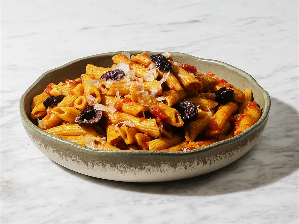 Penne Arrabbiata von HR Italy: Penne in Arrabbiata-Tomatensoße mit schwarzen Oliven und Parmesan auf einem Marmortisch