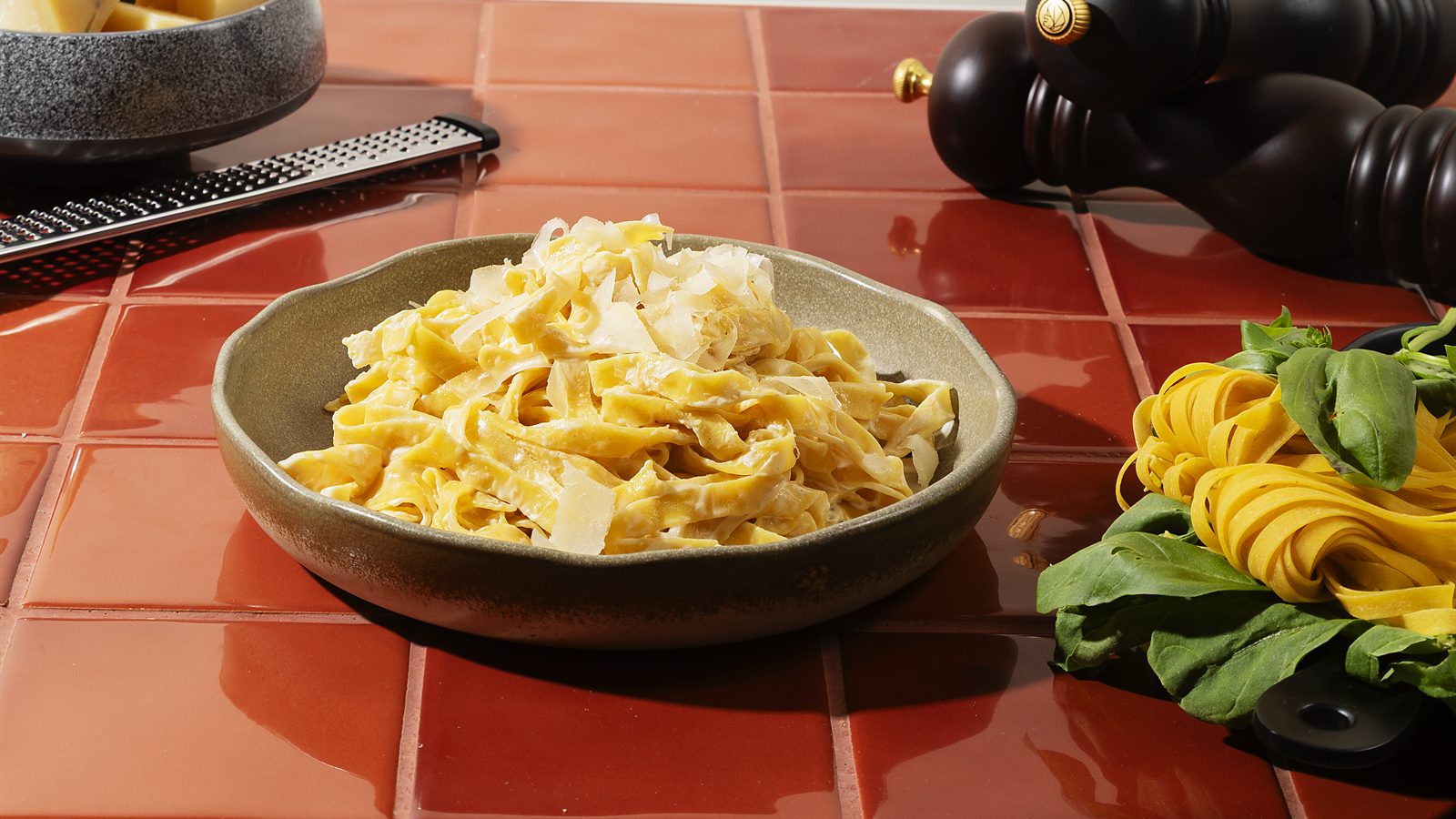 HR Italy Parmesan Kremalı Fettuccine: terrakota karolu masada taze fettuccine, yanında parmesan kalıbı ve karabiber değirmeni