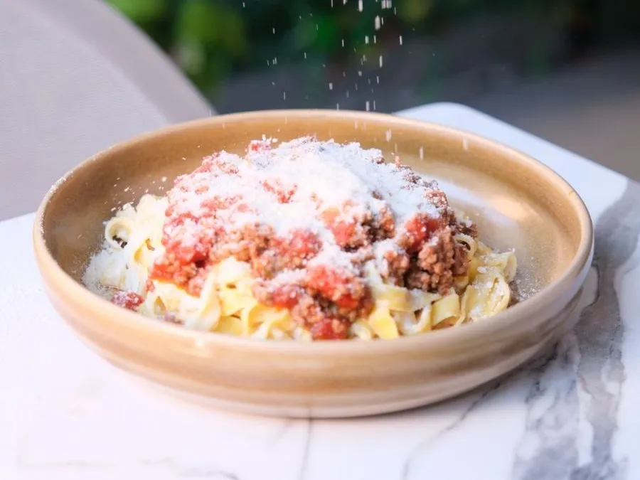 Du parmesan râpé tombe sur des fettuccine à la sauce bolognaise